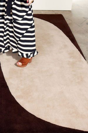 A woman's foot shown standing on a cream, and dark brown area rug by Angela Adams