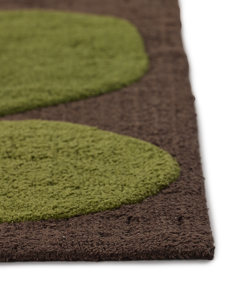A dark brown angela adams "Two Stones Moss" bath mat is viewed from directly above. It features two large, rounded, organic shapes in shades of green: a darker olive green one at the top and a smaller, slightly lighter green one below it. The background of the mat is a soft, textured dark brown.