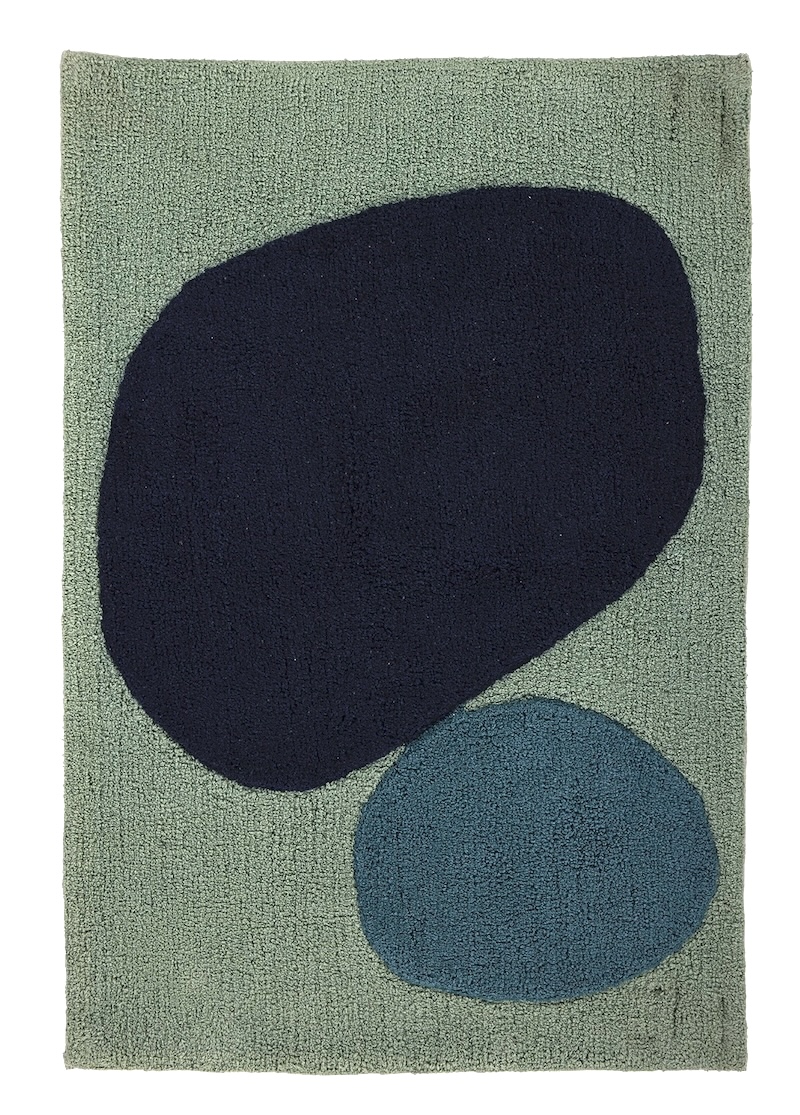 A light teal angela adams "Two Stones Bluebird" bath mat is viewed from directly above. It features two large, rounded, organic shapes: a dark navy blue one at the top and a smaller, lighter blue one below it. The background of the mat is a soft, textured light teal.