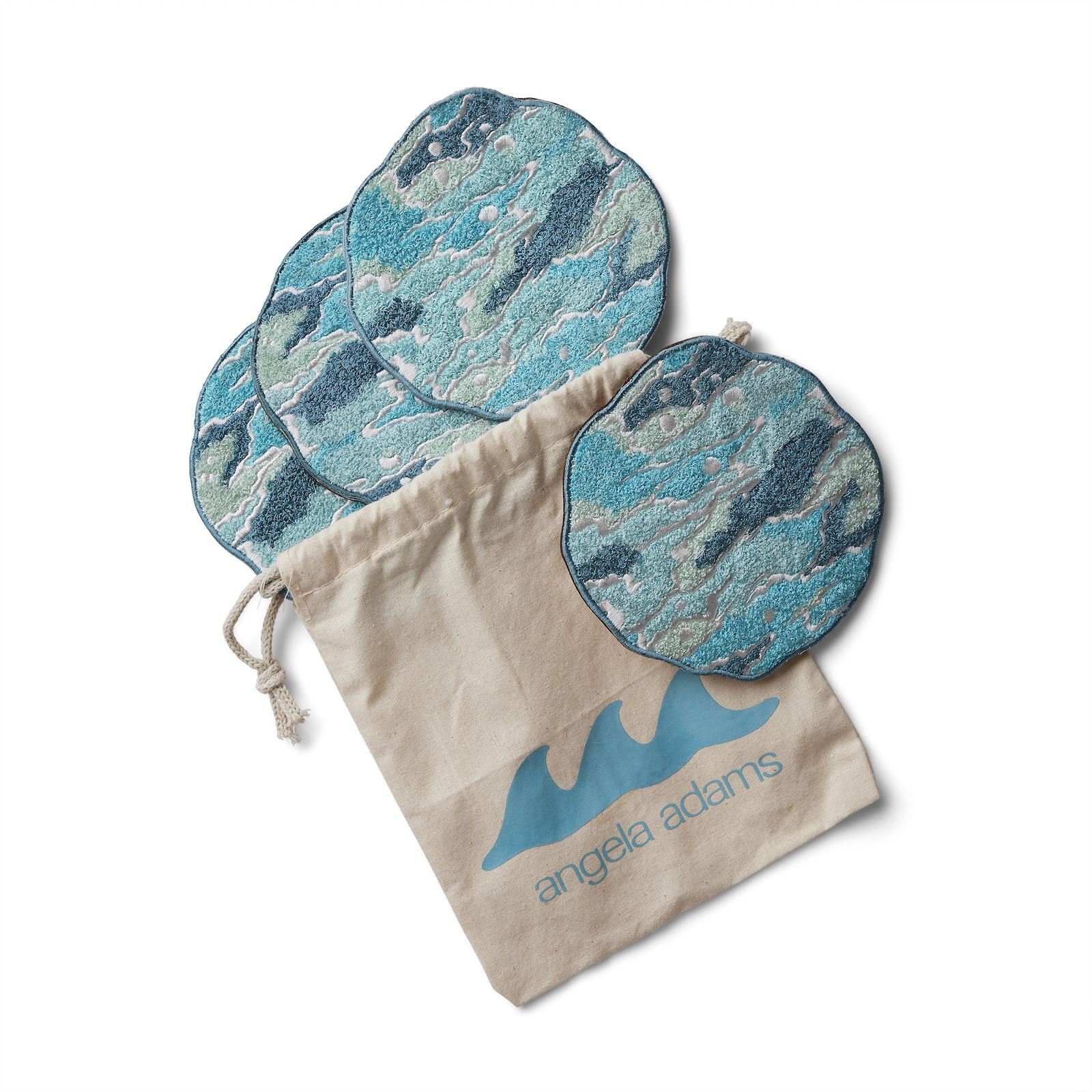 A set of four round, ocean-inspired coasters in shades of turquoise, aqua, seafoam green, and white, designed to resemble swirling waves. The coasters feature a highly textured, tufted surface and are displayed partially inside and spilling out of a natural cotton drawstring pouch. The pouch is printed with the angela adams logo, including stylized blue waves and the brand name beneath. The image is set against a white background for a clean, minimal look.