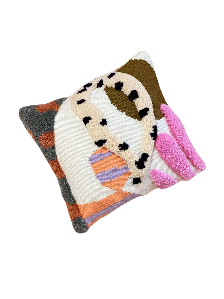 A square decorative throw pillow is shown angled, featuring an abstract, mixed-media design created with various textures and colors. The overall color palette is a mix of neutrals and bright accents. The design is highly geometric and asymmetrical: The center is primarily an off-white or cream color. A thick, tan-colored yarn snake or loop with black spots (resembling an animal print) curves across the center-top. To the top right, a section is filled with a textured dark olive-green/brown. In the lower-center, there is a circular or semi-circular patch with light purple and peach-orange stripes. On the far right, three vertical strips of thick, bright, hot-pink loop texture extend outward. The left and bottom edges feature a border with a dark gray-green texture and patches of burnt orange. The pillow is set against a plain, light-gray background. The surface uses different textile techniques, including flat weaving and various types of high-pile tufting or loop stitching.