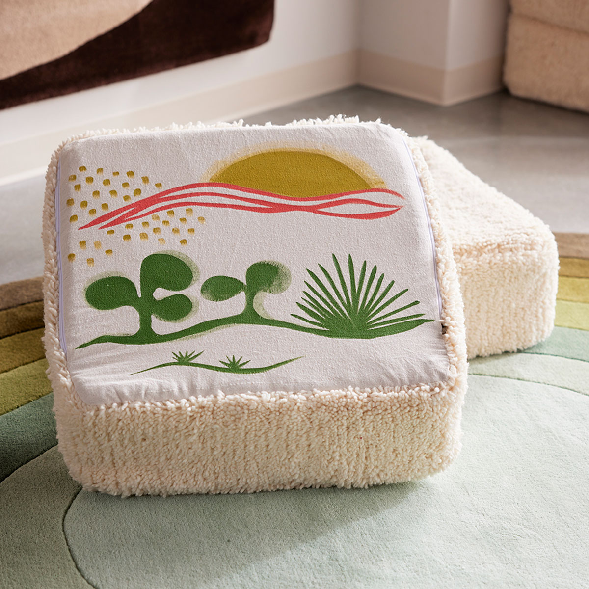 A hand painted, square, wool cushion sits on a custom area rug