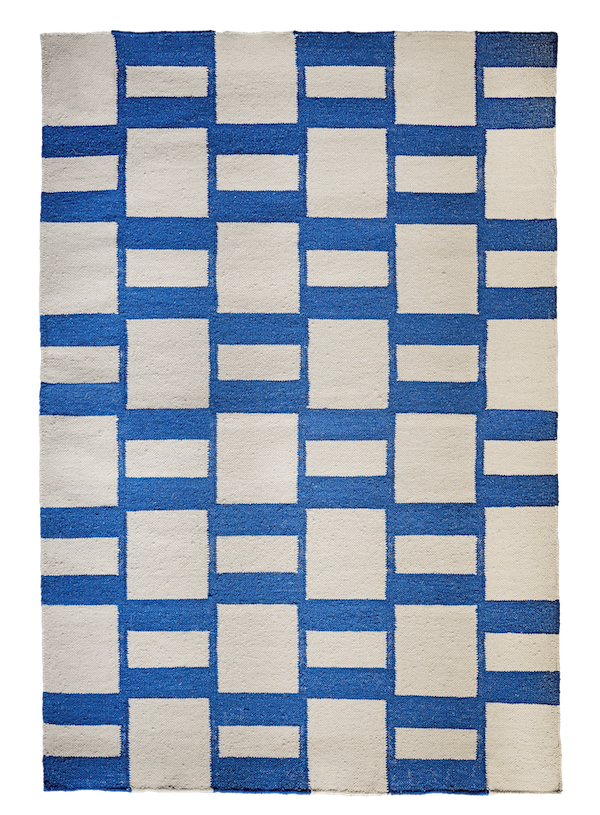 An overhead shot shows a rectangular rug with a grid pattern. The rug's background is a vibrant royal blue. Superimposed on the blue are off-white rectangular and square shapes. The blue forms both horizontal and vertical bands, which in turn frame the off-white shapes. The off-white shapes vary in size and orientation: some are tall and narrow rectangles, others are short and wide rectangles, and some are perfect squares. These off-white shapes are arranged in an alternating pattern, creating a visual rhythm across the rug's surface. The texture appears to be woven and somewhat coarse, possibly wool or a similar natural fiber. The lighting is even, and there are no shadows visible.
