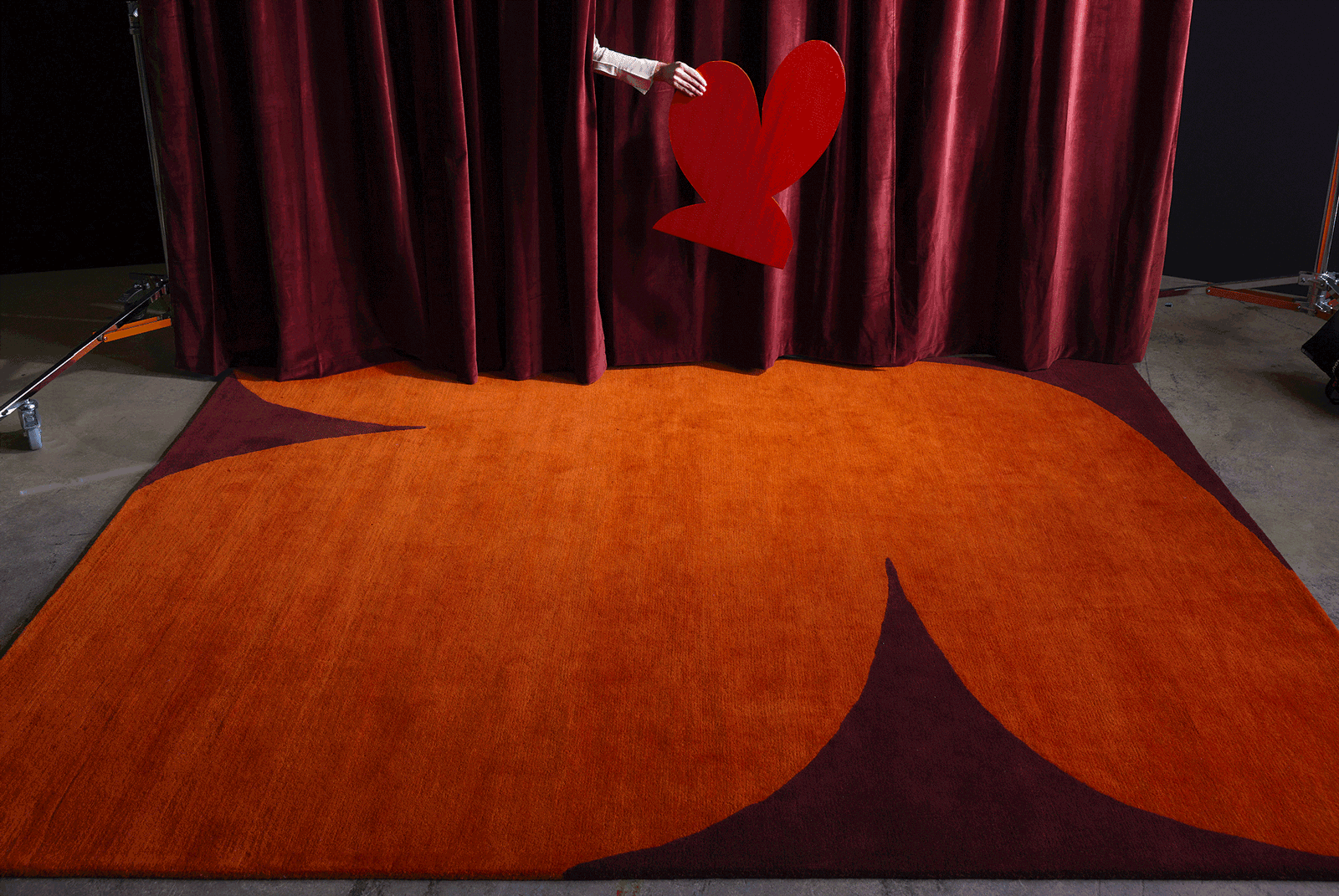A hand wiggles a red heart above the red, Dove Love area rug