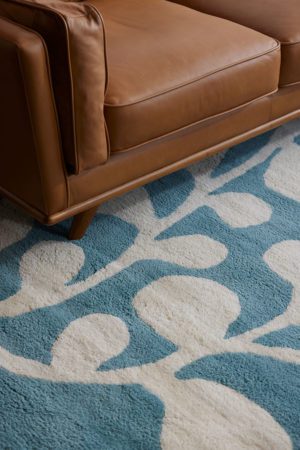 A brown leather chair sits on a neutral and blue area rug with abstract designs on it called Vine Hush